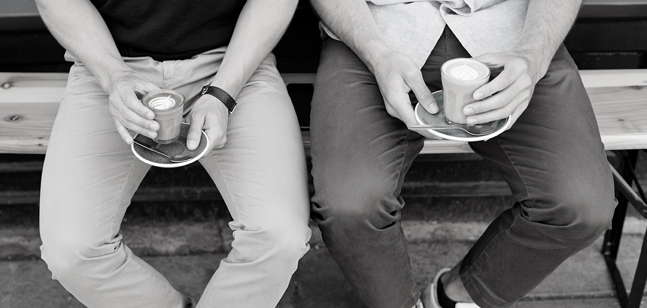 Close Up Of Two Men Sitting Outside Coffee Shop Drinking Coffee